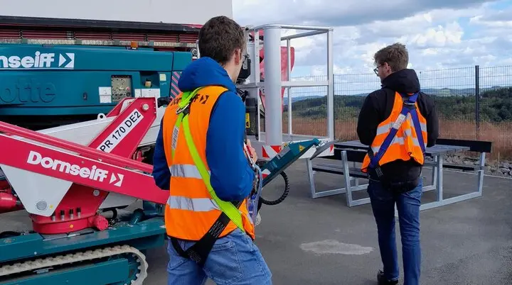 Zwei Personen mit Warnweste laufen prüfend um einen Hubsteiger | © DAV Kletterzentrum Siegerland