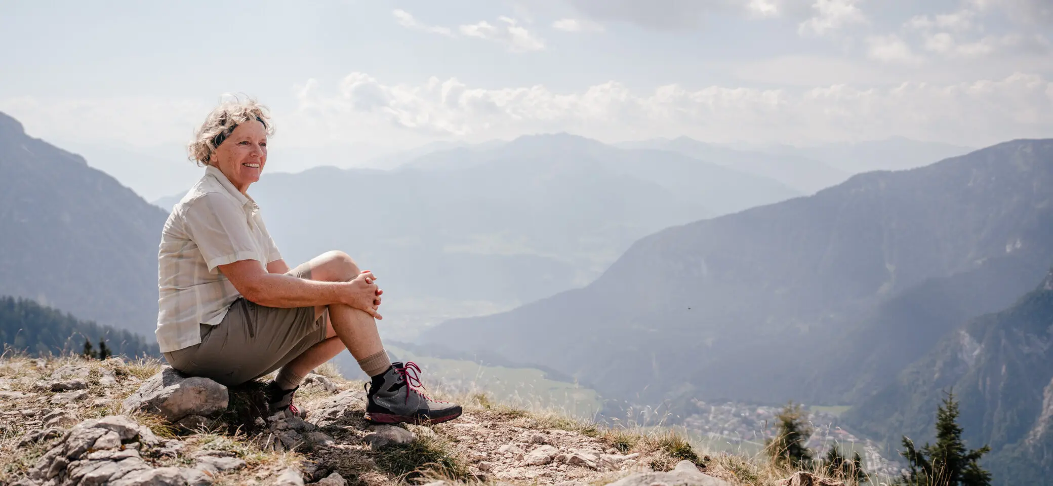 Eine ältere Dame sitzt zufrieden auf einem Felsplateau | © DAV / Marisa Koch