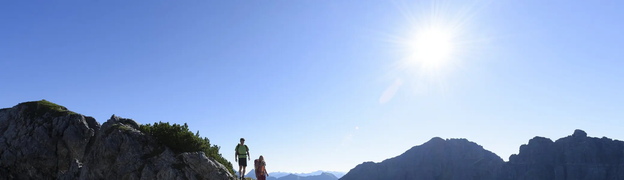 Zwei Wanderer auf einem Felsgrat. Im Hintergrund grüne Bergwiesen | © DAV / Wolfgang Ehn